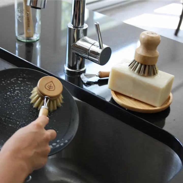 Sisal dish brush cleaning plate and sisal and palm pot scrubber on top of solid dish soap brick.