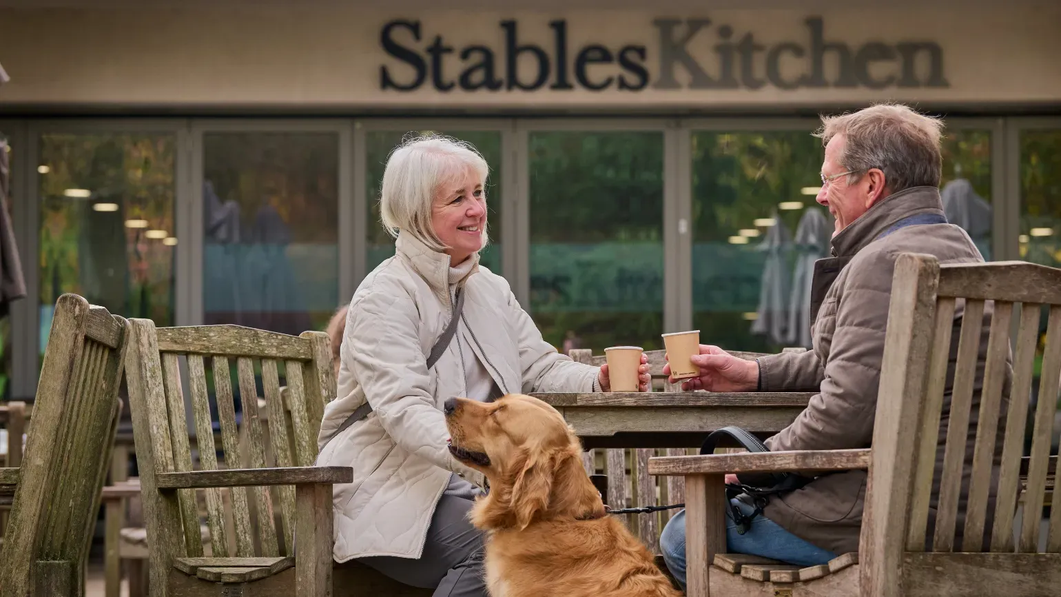 couple drinking hot drinks outside Stables Kitchen with their dog