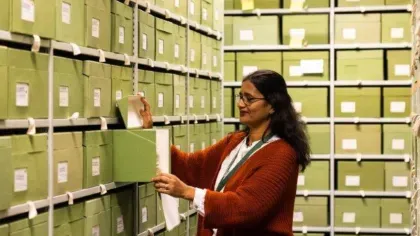A woman selects a specimen box from a shelf filled with green archival boxes at Kew’s Fungarium.