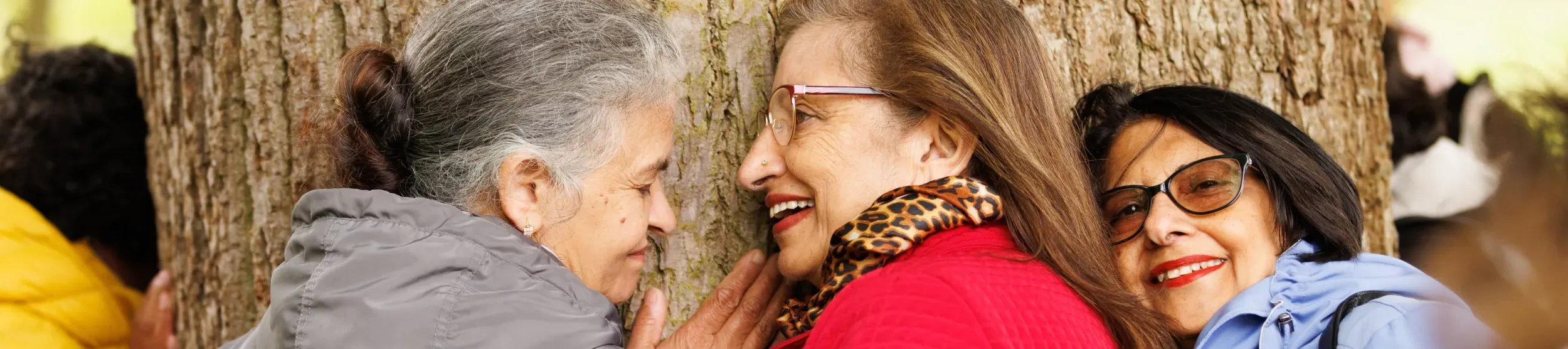 Three women hugging a tree and smiling