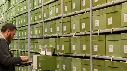 A researcher looking in a green box on a shelf full of green boxes