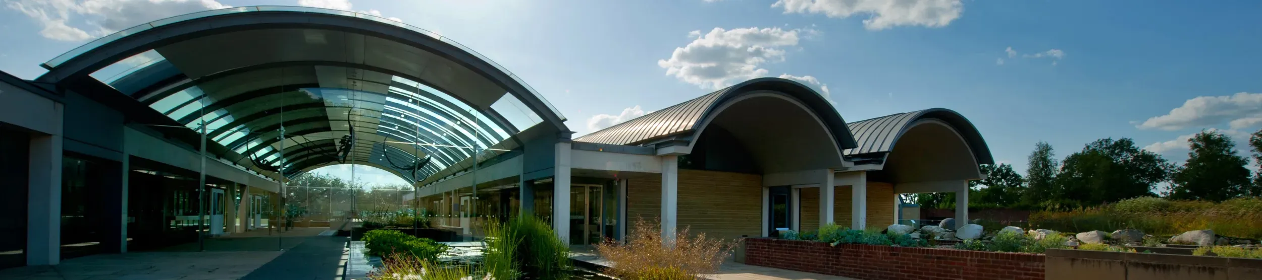 The Millennium Seed Bank at Wakehurst with a large curved glass roof, all under a vibrant blue sky.
