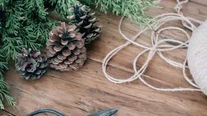 Pinecones and pine needles on a wooden tabletop, arranged with a ball of string and pair of scissors